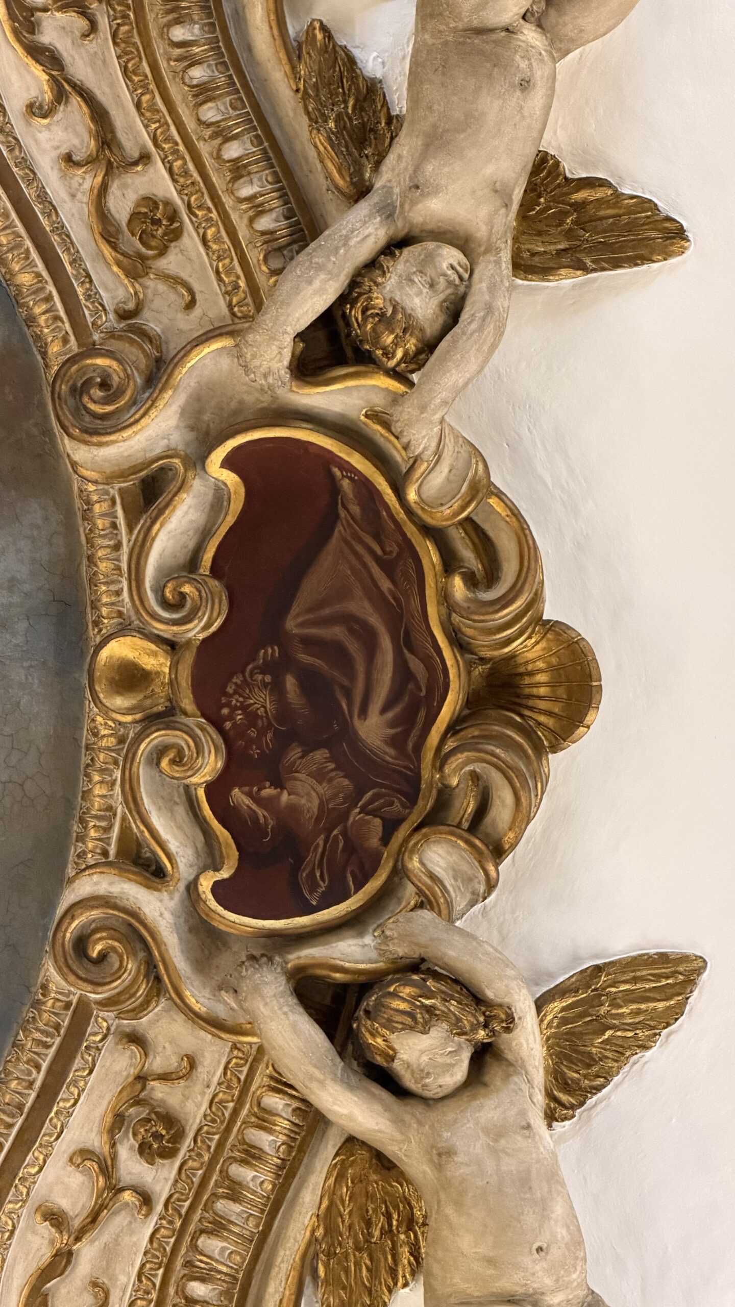Cammeo rosso della cornice sorretto da due putti alati in stucco