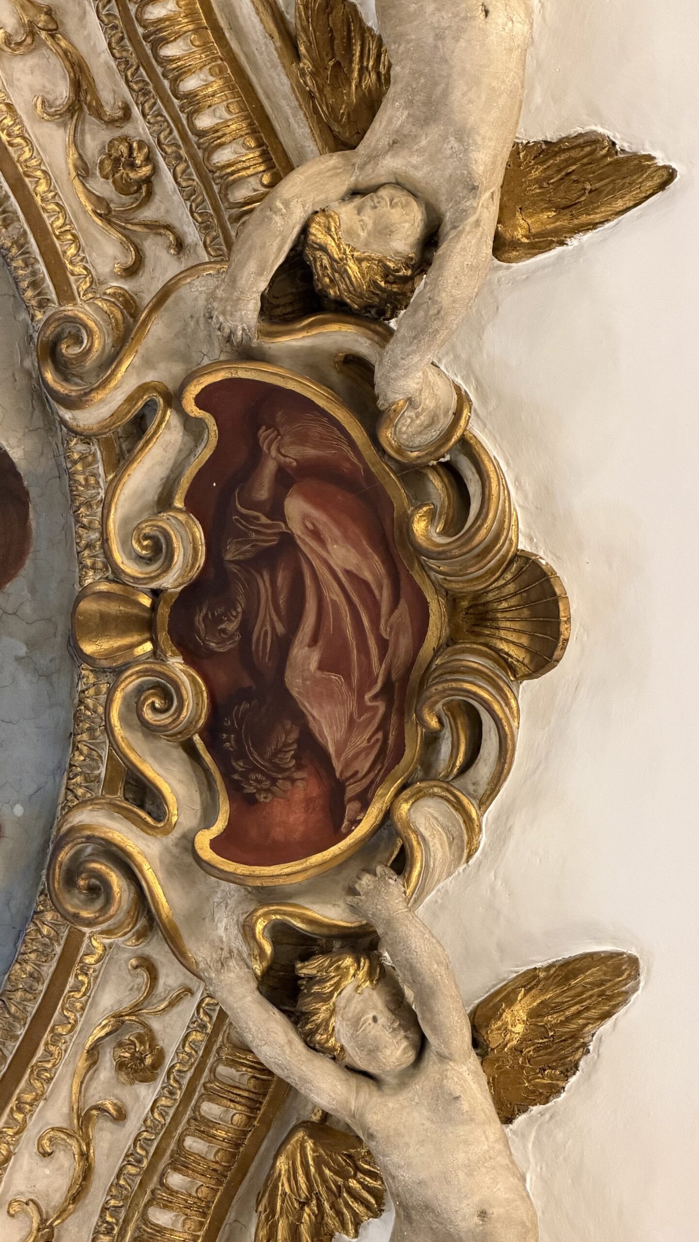 Cammeo su fondo rosso affiancato da putti alati in stucco
